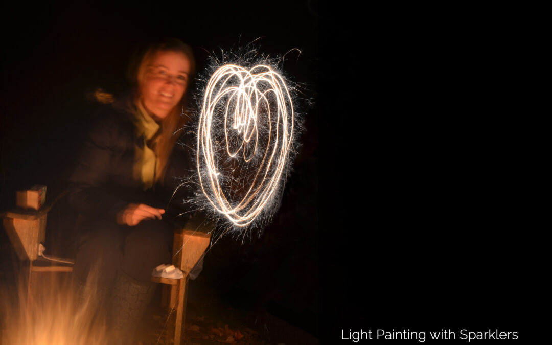 Image of Corinne sitting next to a fire with a heart shape "painted" with a sparkler using time-lapsed photography.